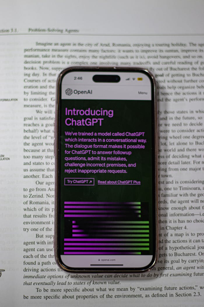 A mobile phone displaying ChatGPT is placed on top of an open book.